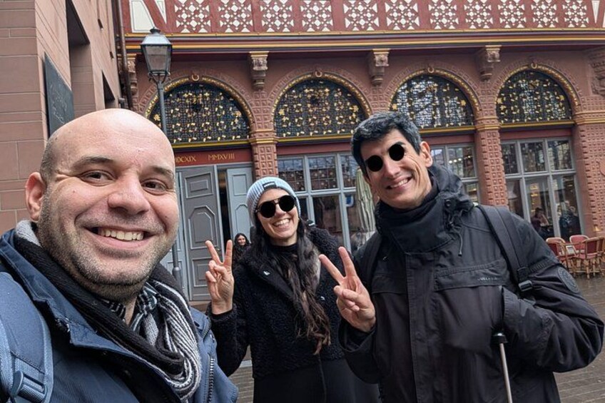 Tre persone che fanno il segno della vittoria davanti a un edificio con finestre e una porta elaborate. 2