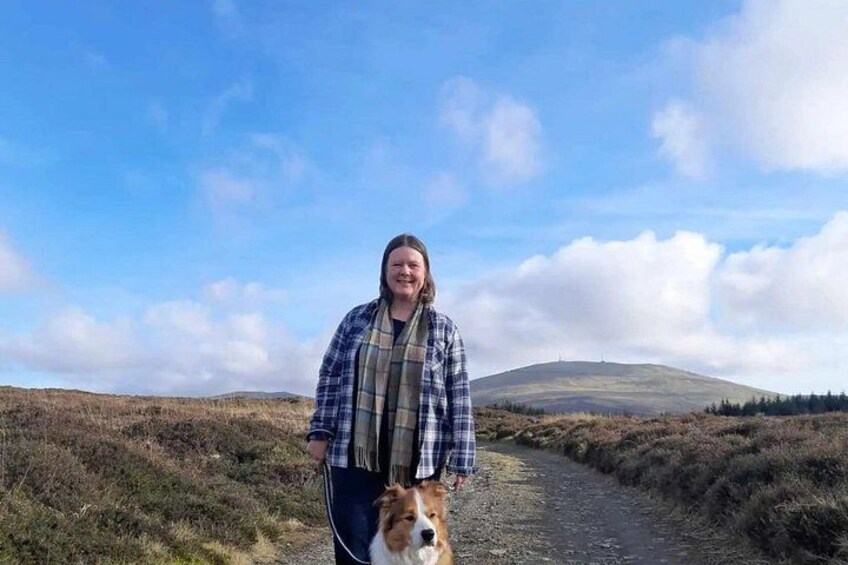 A person walking a dog on a rural path with hills in the background. 3