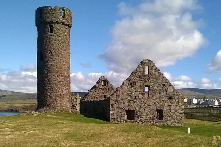A stone tower and ruins in a grassy field with a clear sky. 2