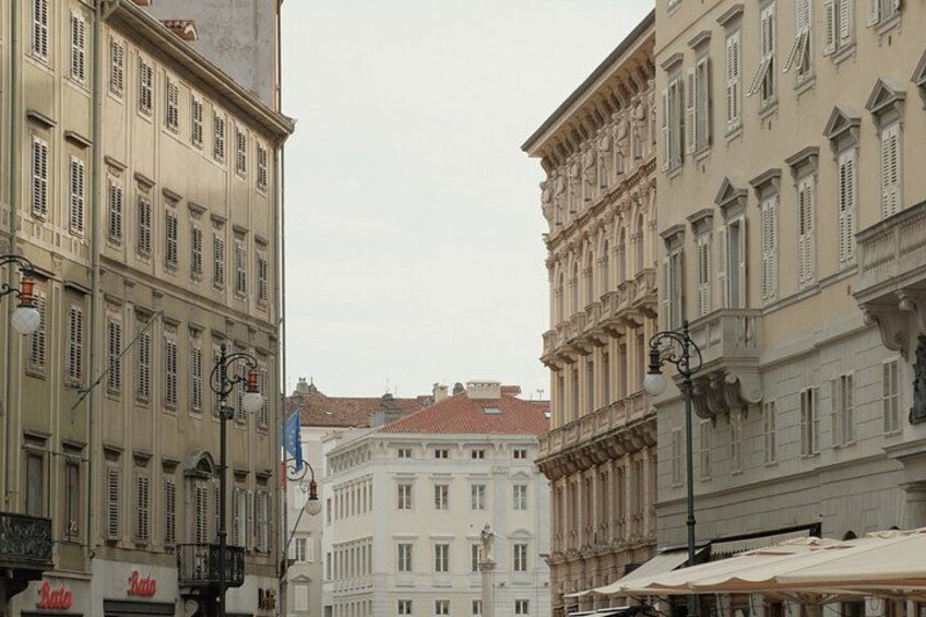 A street with historic buildings, a red-roofed building in the center, and a blue flag. 2