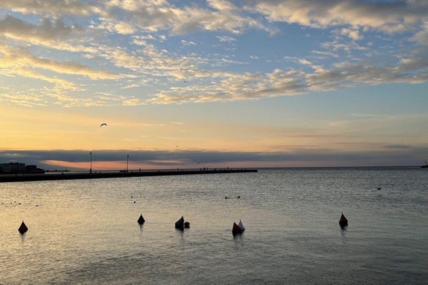 A sunset over a calm sea with buoys and a distant pier. 3