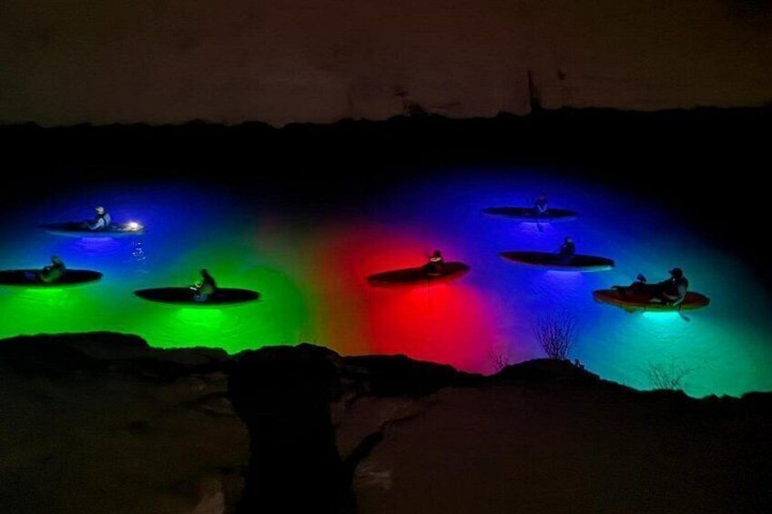 Kayakers on a calm body of water at night, illuminated by colorful lights. 2