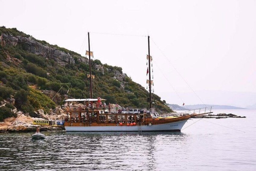 Un barco de vela tradicional amarrado cerca de una costa rocosa con montañas al fondo. 2