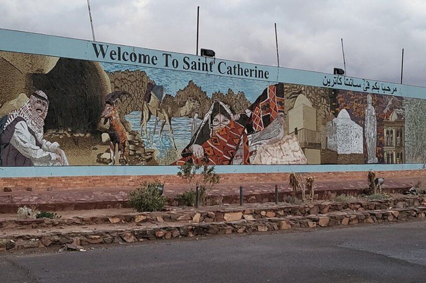 A mural with the text 'Welcome To Saint Catherine' and various figures and scenes. 1
