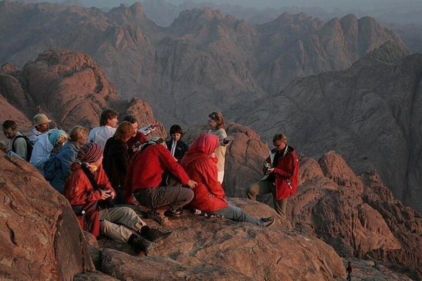 A group of people sitting on a rocky mountain ledge. 3
