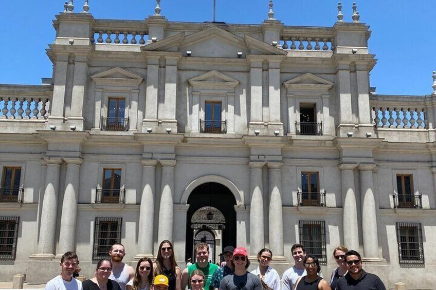 A group of people in front of a large, ornate building with columns and a central archway. 3