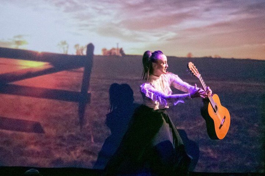 En person som spelar gitarr på en åker med ett staket i bakgrunden. 4