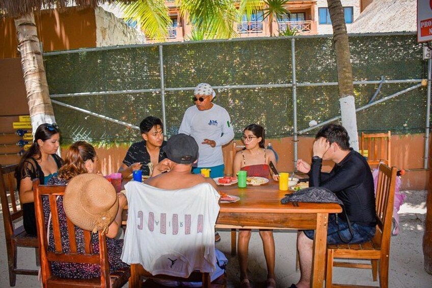 A group of people sitting around a wooden table outdoors, engaged in conversation. 3