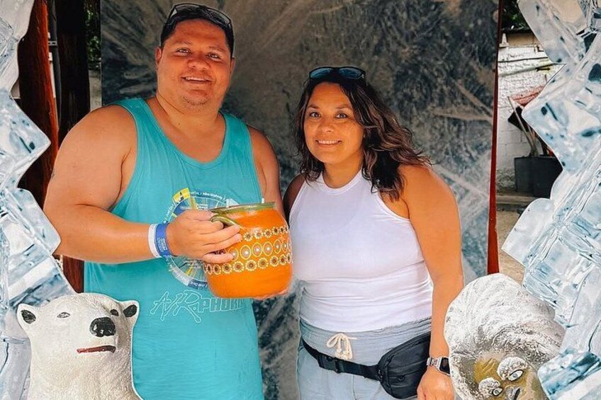 A person holding a patterned container, another person in a white tank top, and a bear statue. 5