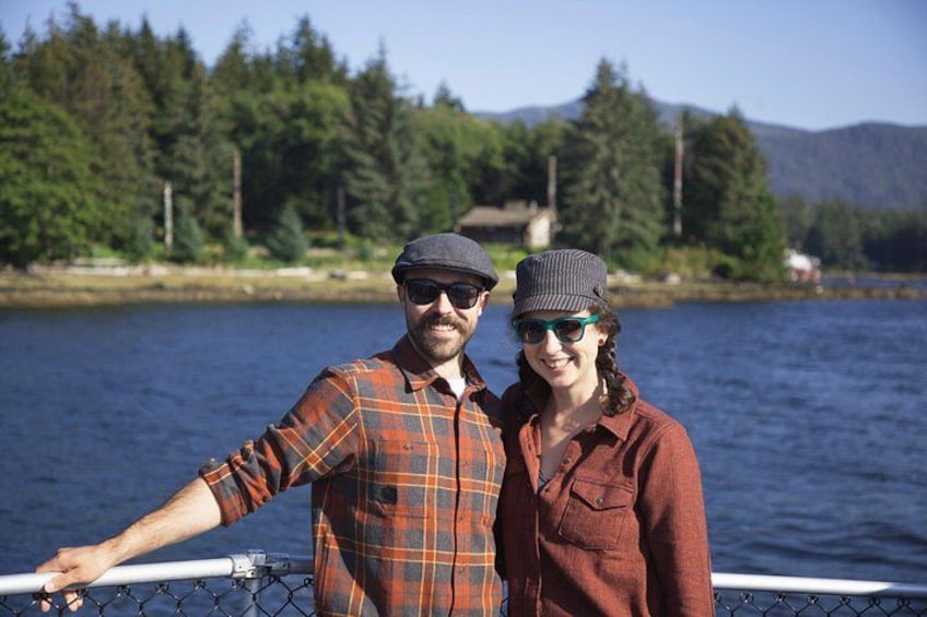 Two people standing on a boat with a forest and mountains in the background. 5