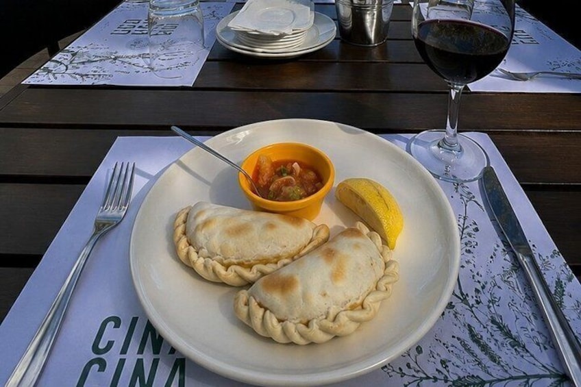 A plate with two empanadas, a bowl of salsa, and a lemon wedge on a wooden table. 3