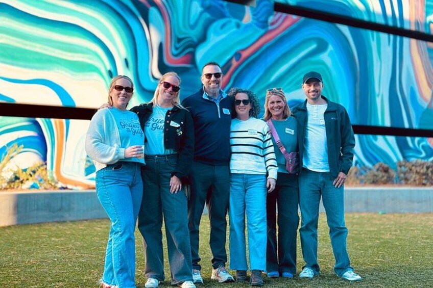 Un groupe de personnes se tient devant une fresque murale abstraite aux couleurs vives. 2