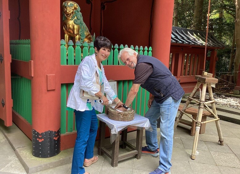Two people interacting with a traditional wooden structure, possibly a shrine, with a golden lion statue and a green fence. 5