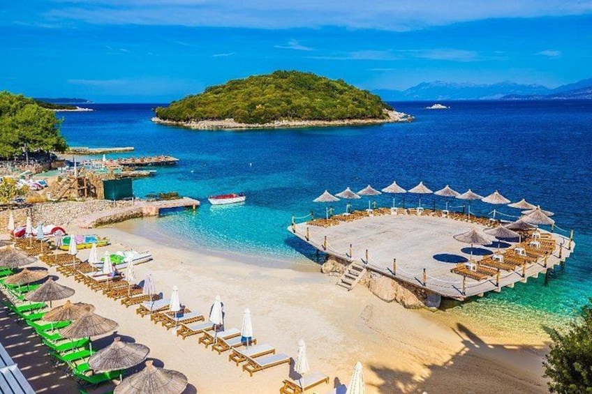 A beach with lounge chairs, umbrellas, and a circular seating area. 1
