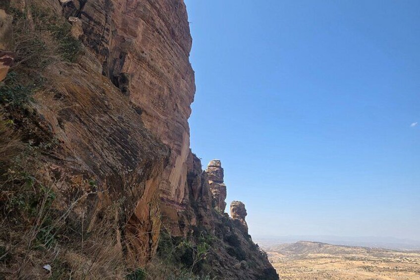 A rocky cliff with a clear sky and distant landscape. 2