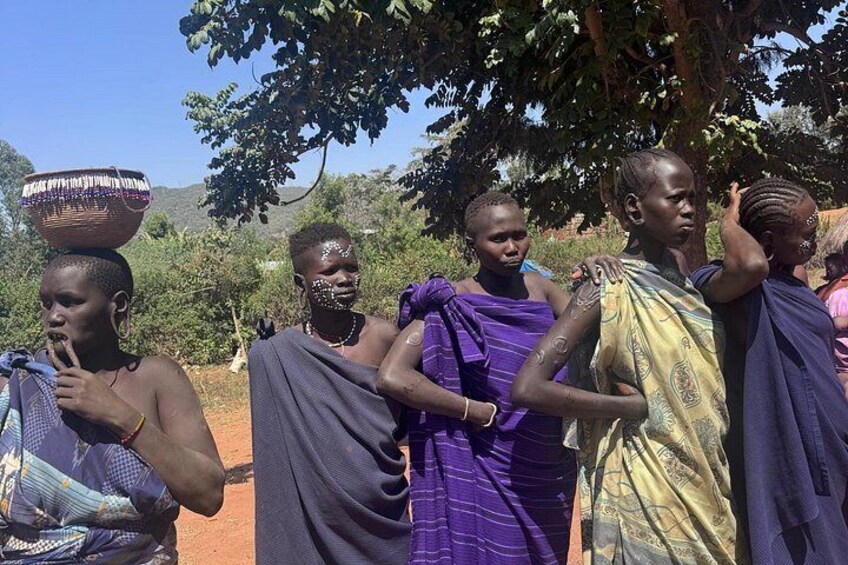 A group of people in traditional attire standing outdoors with trees and hills in the background. 4