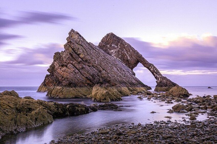 A rock formation with a natural arch over a river. 1