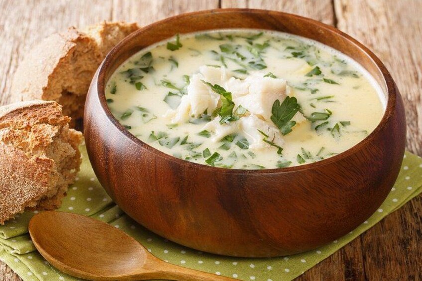 A wooden bowl of creamy soup with herbs, accompanied by a spoon and a piece of bread on a green napkin. 4