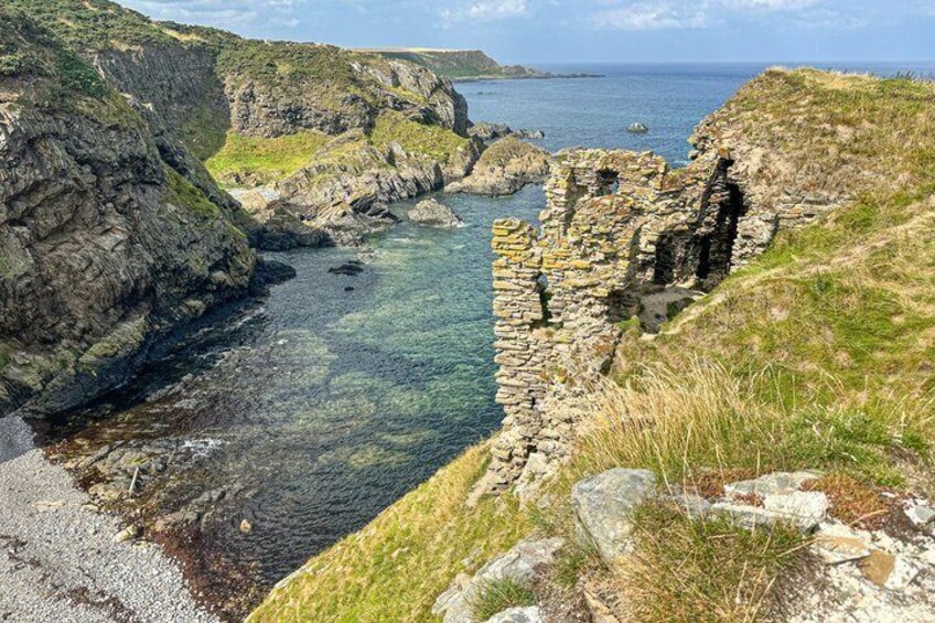 A coastal landscape with a stone structure, rocky cliffs, and clear water. 2