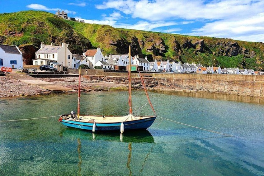 A small boat moored in clear water near a coastal village with houses and a hill in the background. 3