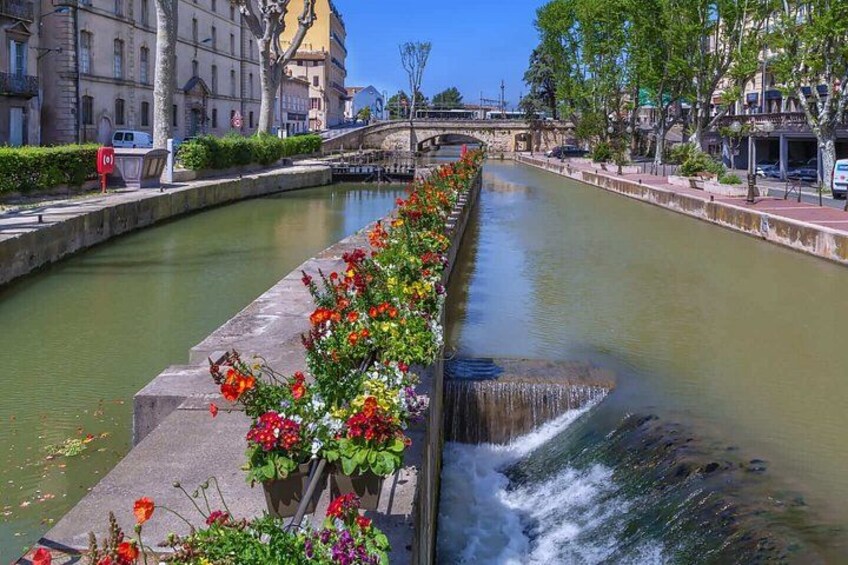 A canal with a waterfall, lined with colorful flowers, and buildings in the background. 5