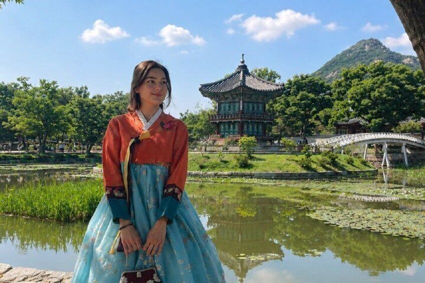 A person in traditional attire standing by a pond with a pagoda and bridge in the background. 3