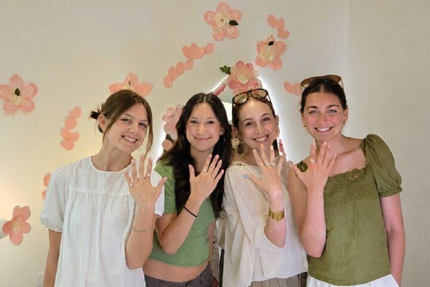 Four people posing with their hands raised in front of a wall decorated with pink flowers. 1