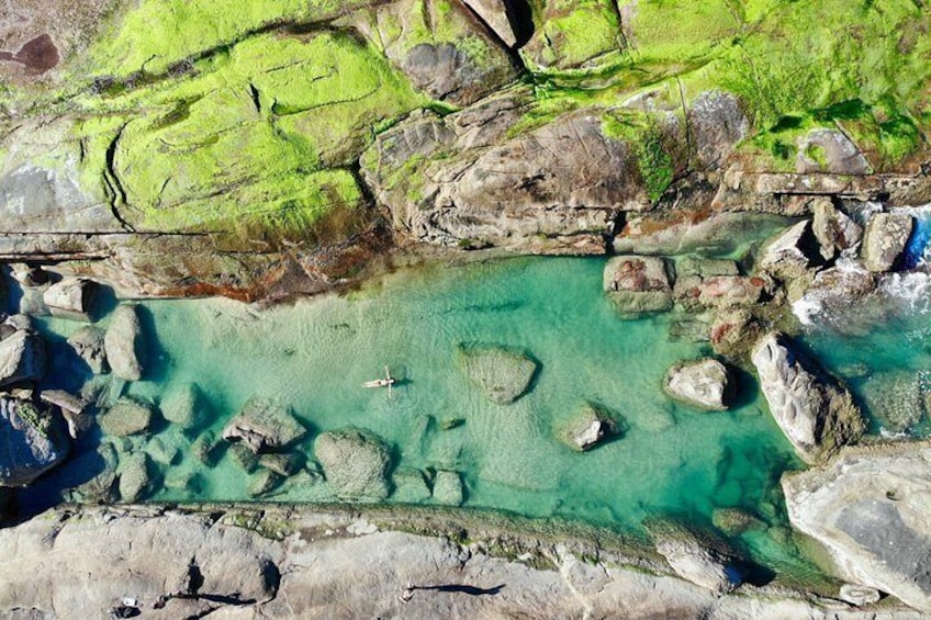 A coastal landscape with clear turquoise water, rocky formations, and green moss-covered terrain. 1