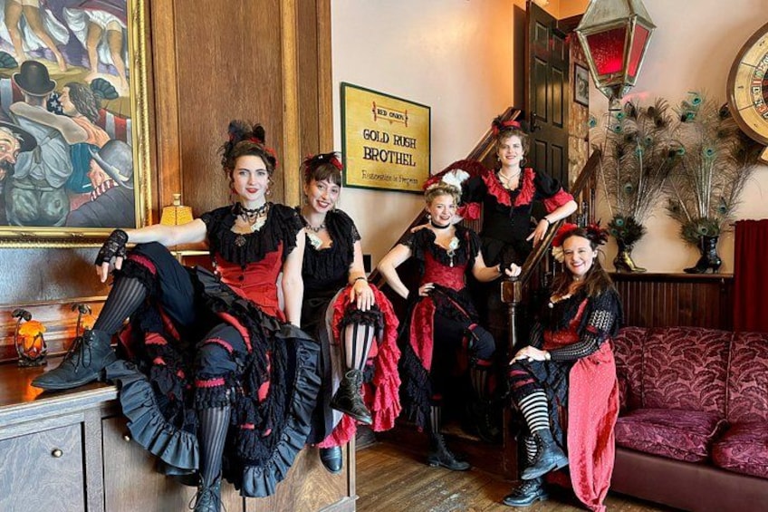 Un groupe de personnes vêtues de costumes de l’époque victorienne est assis sur un canapé et devant un meuble en bois. 1