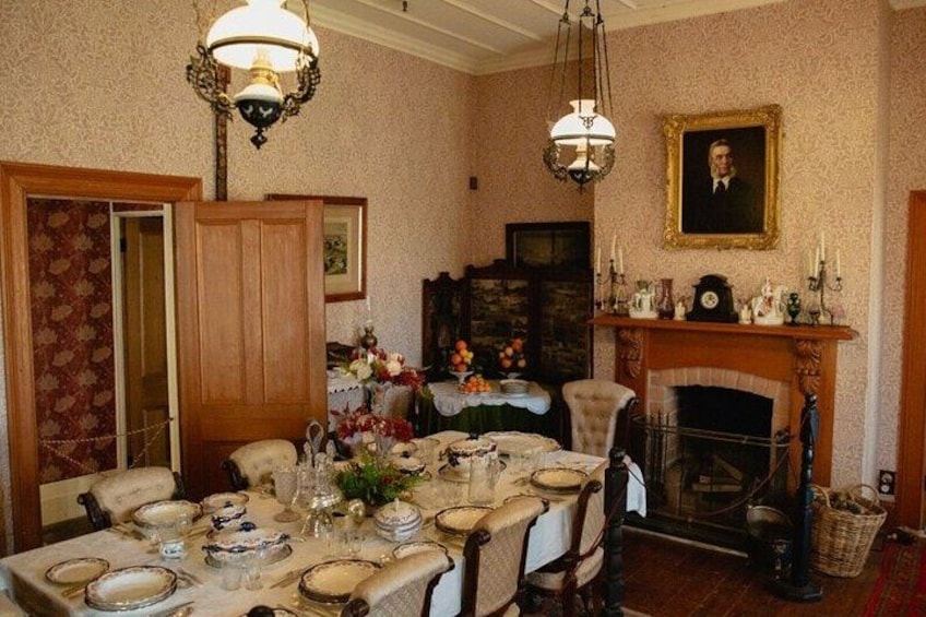 A dining room with a wooden table set for a meal, a fireplace, and a portrait on the wall. 4
