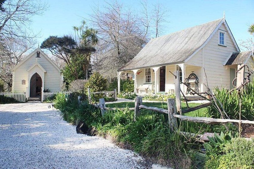 A white building with a porch, surrounded by greenery and a gravel path. 5