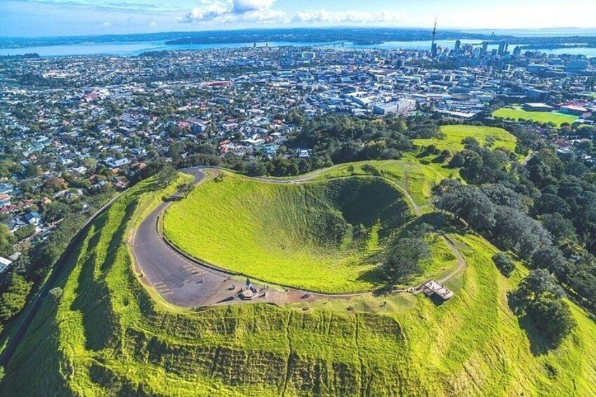 An aerial view of a green hill with a circular clearing surrounded by a road. 3