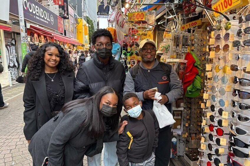Un groupe de personnes se tient dans un marché où sont vendus divers articles, notamment des lunettes de soleil et des sacs. 4