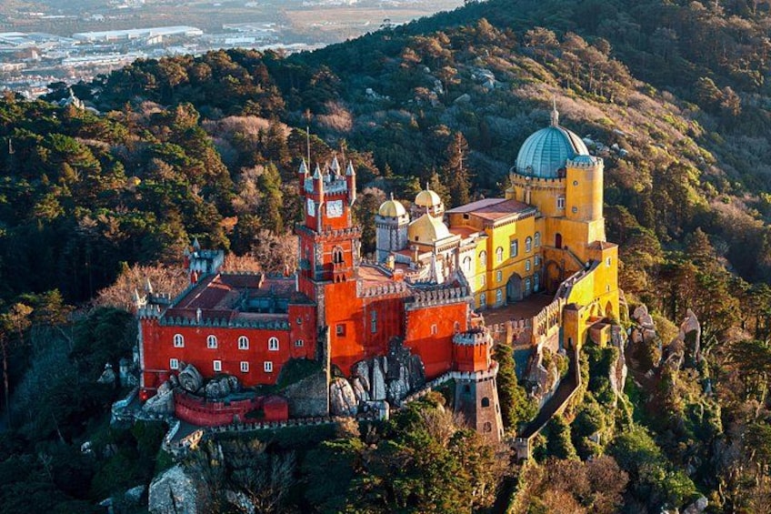 Un castillo con edificios rojos y amarillos, rodeado de vegetación y colinas. 1