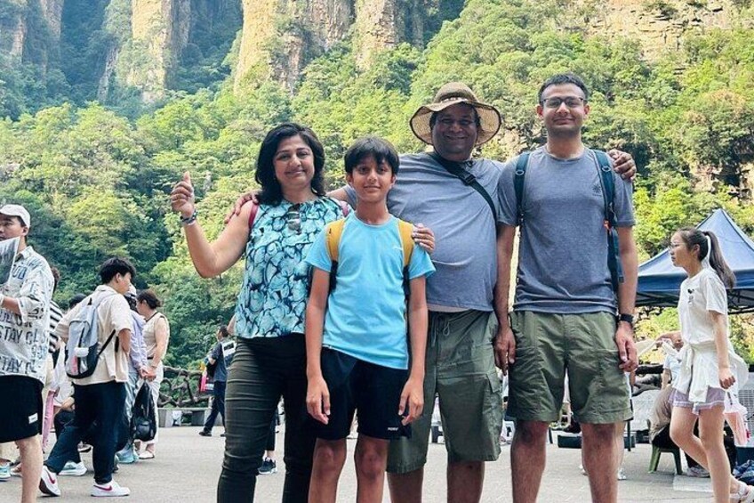 A group of people standing in a natural setting with greenery and rocky cliffs in the background. 1