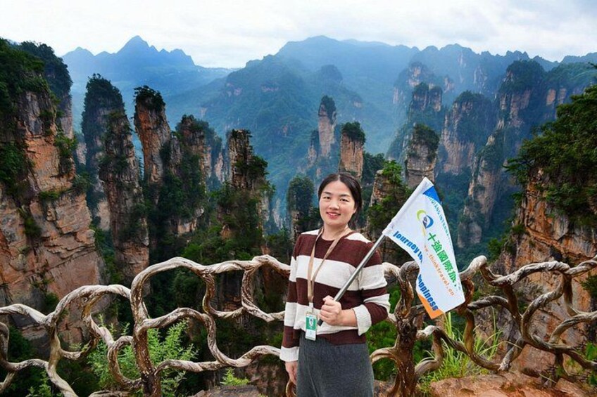A person standing on a rocky outcrop with a flag, surrounded by tall, narrow rock formations and greenery. 2