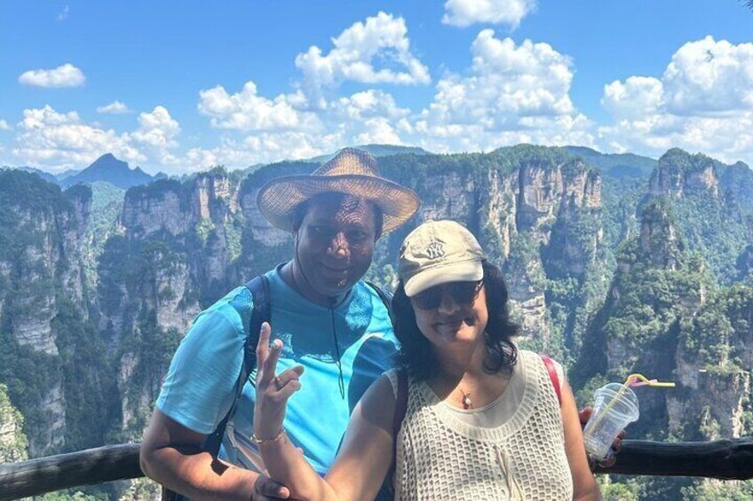Two people standing on a viewing platform with a mountainous landscape in the background. 3