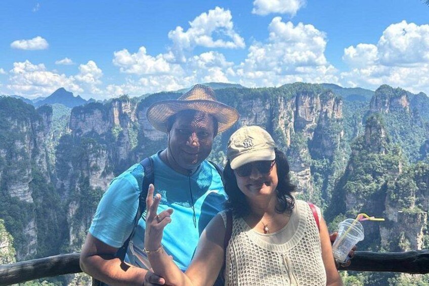 Two people standing on a viewing platform with a mountainous landscape in the background. 3
