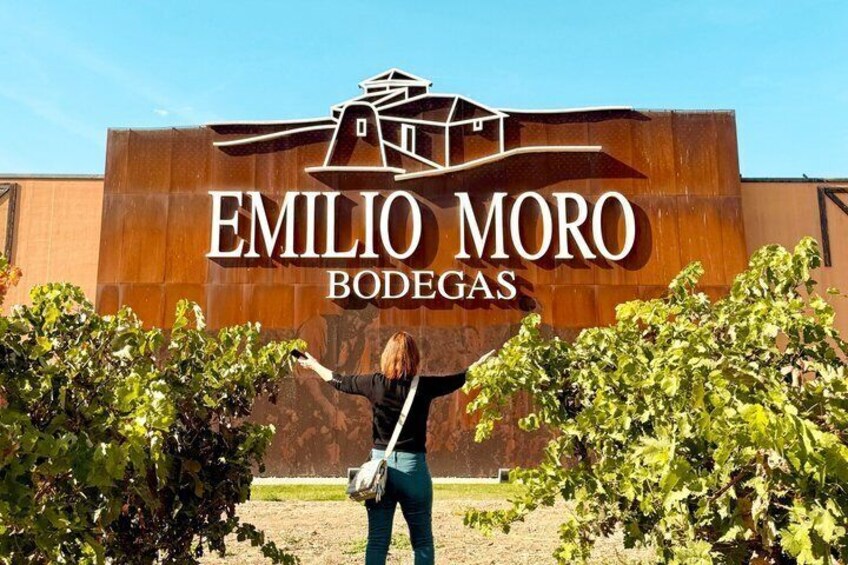 A sign for Emilio Moro Bodegas with a woman pointing at it. 2