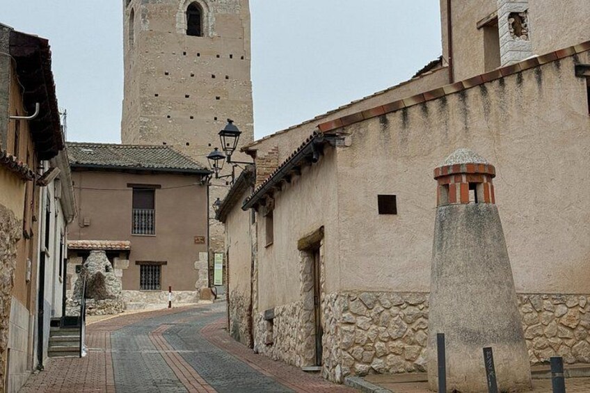 A narrow street with stone buildings, a tall tower, and a stone monument. 2