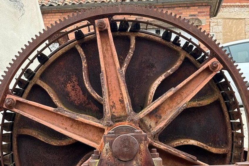 A large, rusted metal wheel with spokes and teeth along the rim, likely part of an old machine or structure. 3