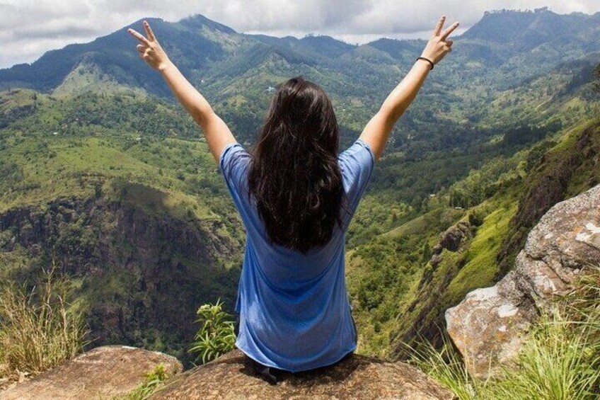A person sitting on a rock with arms raised, overlooking a mountainous landscape. 1