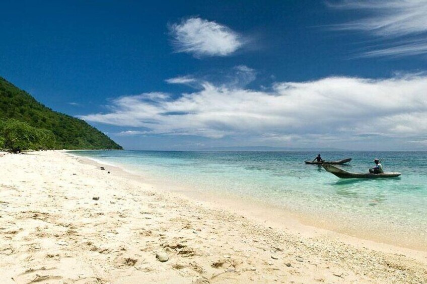 A beach with clear turquoise water, a sandy shore, and two boats with people in them. 5