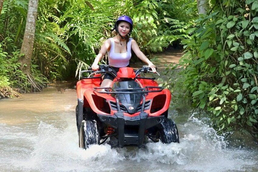 A person riding an ATV through a shallow water crossing surrounded by dense greenery. 5
