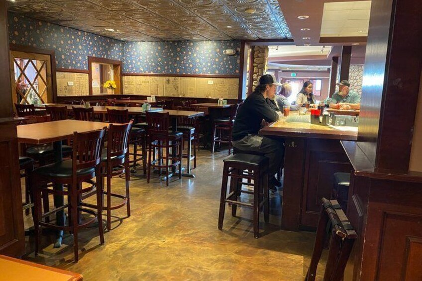 A restaurant interior with wooden tables and chairs, a bar area, and a patterned ceiling. 5