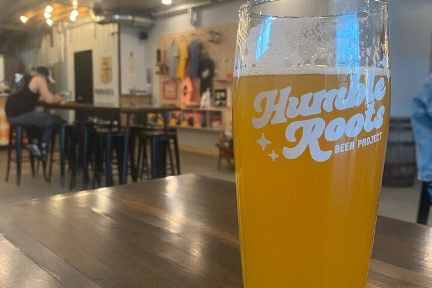 A glass of beer with 'Humble Roots Beer Project' on it, placed on a wooden table in a casual dining setting. 4
