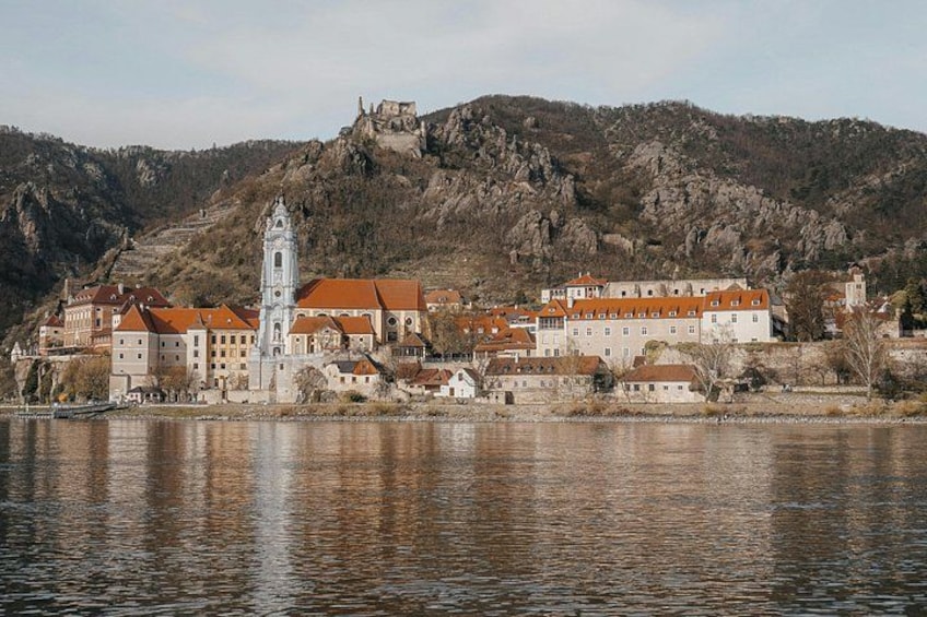 A historic town by a river with a prominent church tower, a castle on a hill, and traditional buildings. 5