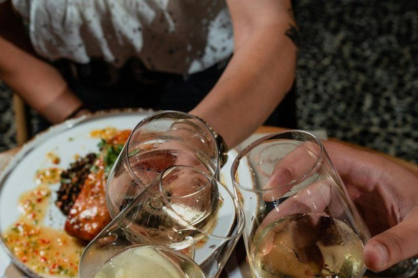 A person holding three wine glasses with a plate of food in the background. 3