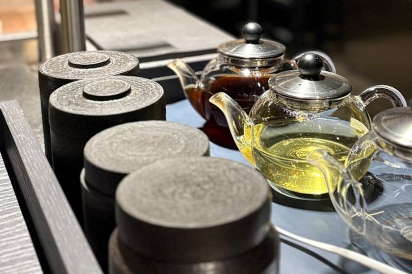 Ein Tisch mit schwarzen zylindrischen Objekten, eine Glas-Teekanne mit Deckel und eine Teetasse aus Glas. 5