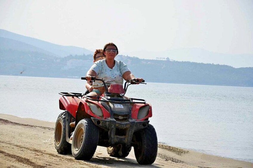 A person riding a red ATV on a sandy beach with a lake and mountains in the background. 1